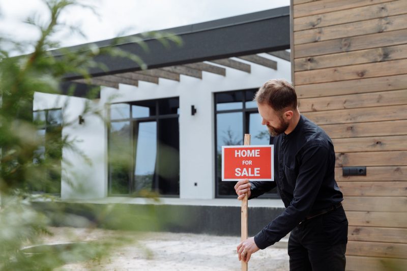 Man placing a home for sale sign outside a modern house for real estate listing